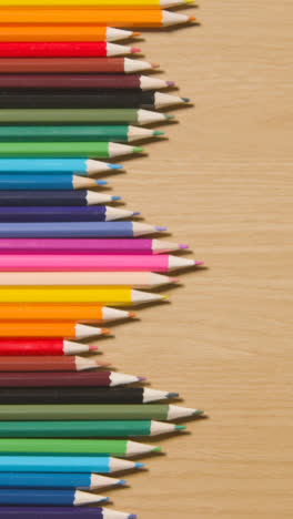 Vertical-Video-Of-Coloured-Pencils-Arranged-In-A-Symmetrical-Pattern-On-Wooden-Background